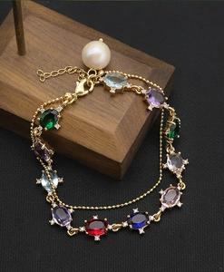 Macro shot of colorful oval gemstones and a large white pearl on a gold-plated bracelet