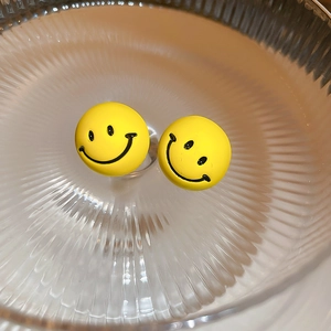 Close-up of bright yellow smiley face stud earrings on a textured glass tray