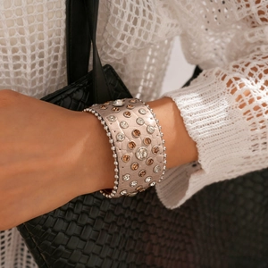 Détail d'un large bracelet en cuir beige orné de cristaux et de perles argentées
