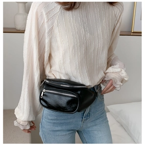 Detail of black leather waist bag with silver zippers shown on a model in a home setting
