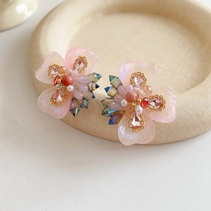 Détail rapproché de boucles d'oreilles fleurs avec pétales en résine rose et cristaux