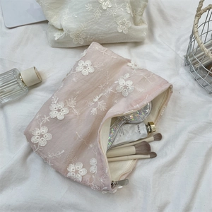 Detail showing pink lace mesh makeup bag with floral embroidery and gold zipper closure