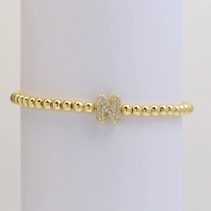 Macro view of gold beaded bracelet with zircon pave letter N charm on white stand