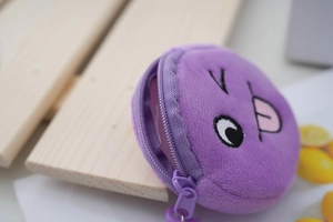 Close-up of a purple plush coin purse with embroidered cartoon face on wood surface