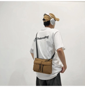 Back view of a khaki nylon messenger bag styled with a white graphic t-shirt and headphones