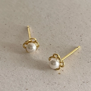 Detailed view of pearl flower stud earrings in gold-tone metal on a textured background