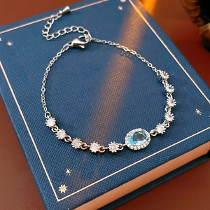 Detail shot of a silver floral bracelet with an oval blue stone and lobster clasp closure