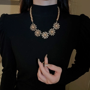 Detailed close-up of a floral pearl necklace featuring golden daisies on a black turtleneck