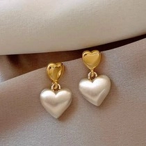 Nahaufnahme goldener Herzstecker mit großen Perlenherz-Anhängern auf beige Faltenstoff