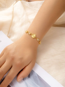 Detail of gold clover bracelet with sunburst texture and baguette-cut emerald zirconia