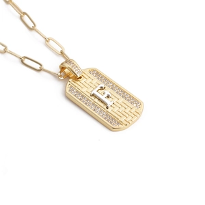 Détail d'un pendentif rectangulaire doré avec une lettre F argentée et des cristaux