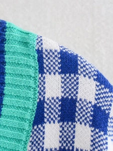 Macro view of blue and white checkered knit sweater with green ribbed edge texture