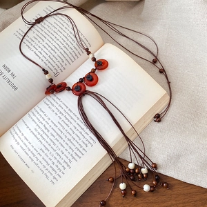 Dettaglio della collana boho con perline di legno, anello di agata rossa e nappa su libro