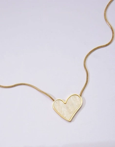 Detail view of a gold snake chain necklace with a marble textured heart pendant