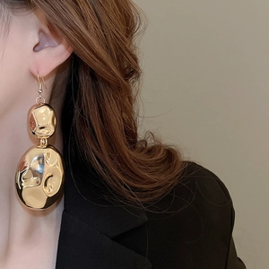 Close-up of model wearing gold irregular crinkle earrings with polished metallic texture