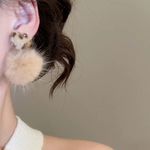 Detail of leopard print heart earrings with brown pompom pendant on a model