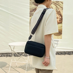 Fashionable black PU leather crossbody bag worn by a model in a minimal outdoor setting