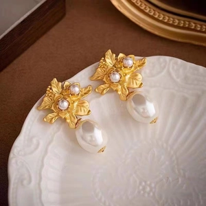 Gros plan de boucles d'oreilles fleurs dorées avec perles baroques sur plat céramique