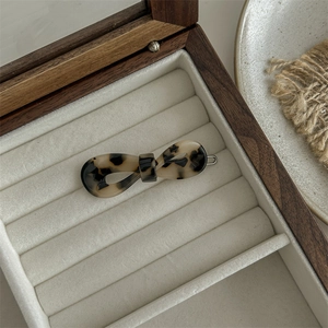 Detailed close-up of a leopard print acetate bow hair claw clip in a wooden jewelry box