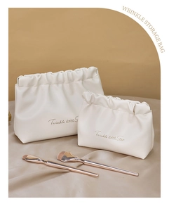 Detailed view of two white pleated PU leather makeup bags with golden lettering and brushes
