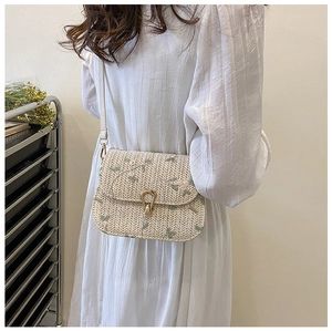 Detail of woven straw crossbody bag with green floral embroidery and gold horseshoe buckle