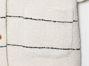Dettaglio del tessuto della giacca in tweed bianco con strisce nere e bottoni dorati