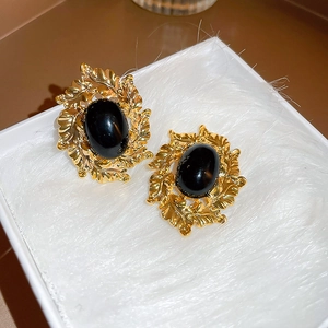 Close-up of vintage golden leaf earrings with black oval stones on white plush fabric