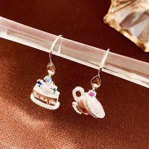 Detail of silver asymmetric earrings featuring a tiered cake and teapot with colored gems