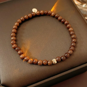 Macro detail of dark agarwood prayer beads with a carved gold bead on leather surface