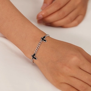 Detail of silver chain bracelet with black butterfly pendants on a model's wrist
