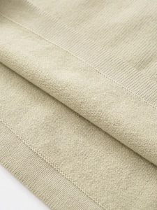 Dettaglio macro della trama in maglia verde salvia con bordo a coste e materiale morbido