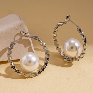 Detail view of silver hoop earrings with white faux pearls on a beige textured surface