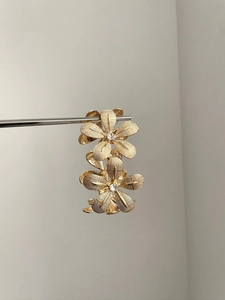 Detail of golden floral earrings featuring textured petals and sparkling zircon centers
