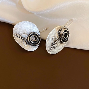 Macro detail of vintage silver earrings featuring a relief rose and matte metal texture