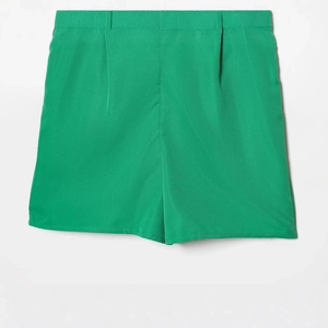 Flat lay of women's high-waisted green shorts with ruffle details and pleated waist
