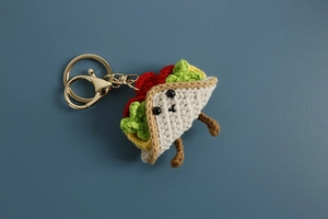 Detail of handmade crochet taco keychain with smiling face and golden lobster clasp