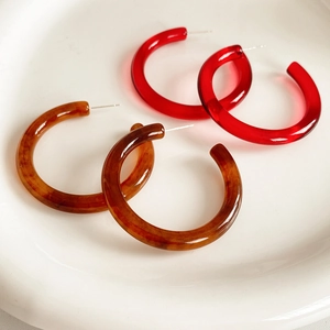 Dettaglio di orecchini a cerchio a C in resina rossa e ambra su un piatto bianco