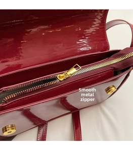 Detail of smooth gold zipper and wine red patent leather on a stylish handbag