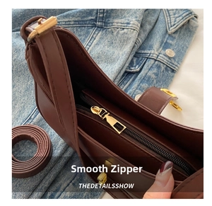 Detail view of smooth golden metal zipper and dark brown leather on underarm bag
