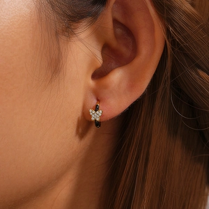 Close-up of golden butterfly earring with black enamel and zircons worn on ear