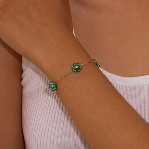 Detail of a gold chain bracelet with green beaded flowers worn on a female wrist