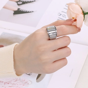 Close-up of wide stainless steel ring with white shell inlay worn in a lifestyle setting