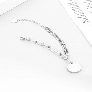 Détail de bracelet argenté double couche avec maille gourmette, trombone et charms ronds