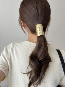 Detail of gold metal ponytail cuff with textured hammered finish on a model