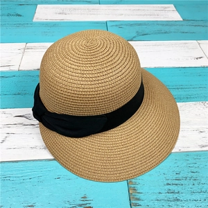 Dettaglio cappello di paglia intrecciato con fiocco nero su fondo di legno blu