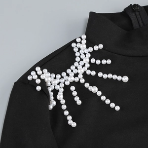 Détail d'une robe noire en maille avec des perles blanches décoratives sur l'épaule