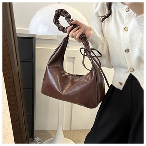 Detail of dark brown faux leather shoulder bag with ruched handle and side ribbon tie