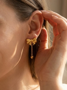 Close-up of golden bow earring with chain tassel and bead on a female model