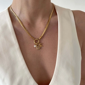 Close-up of gold Cuban chain with pearl, pink heart lock, and letter K charms on a model