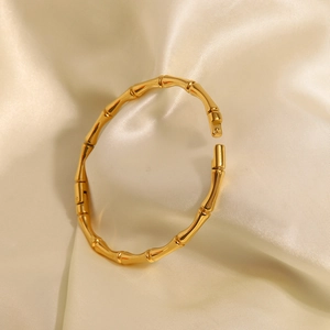 Détail d'un bracelet bambou en acier doré 18 carats sur du tissu en soie crème